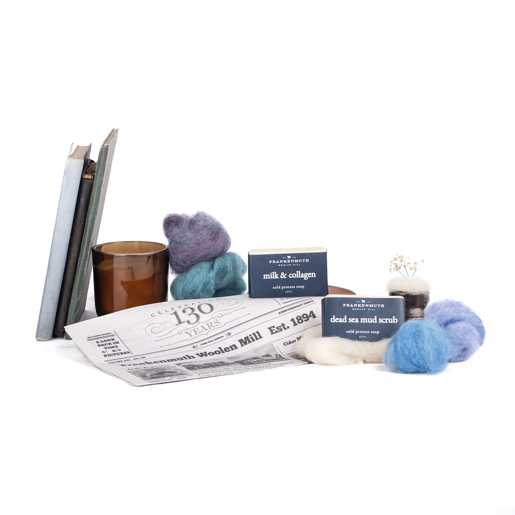 Collection of items including books, a candle, a newspaper, and felted soap products on a white background